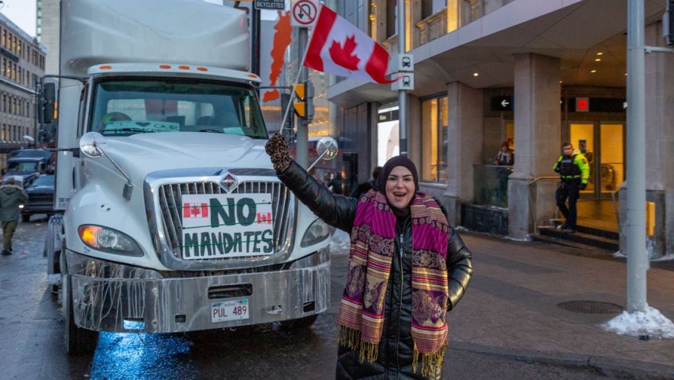Une manifestante tient un drapeau du Canada devant un camion du convoi de la liberté dans les rues d'Ottawa.